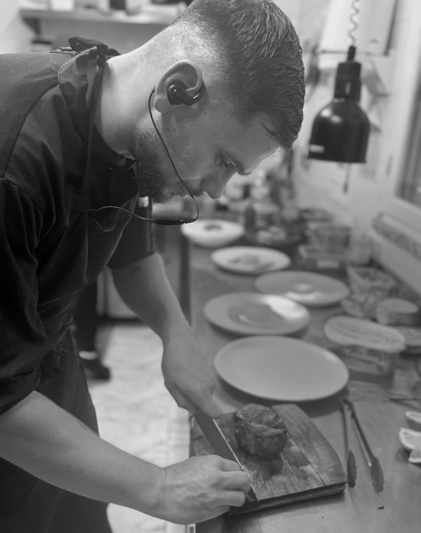Le chef tranche une pièce de viande sur une planche, assiettes alignées devant lui
