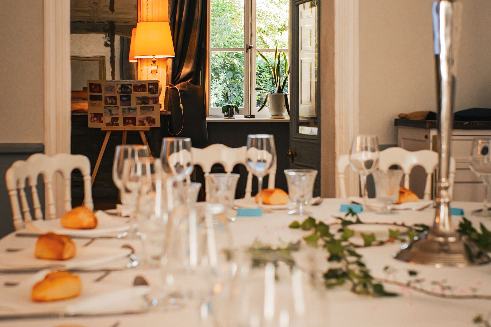 Table dressée dans un salon près d'une fenêtre lumineuse, verres, petits pains et lampe en arrière-plan